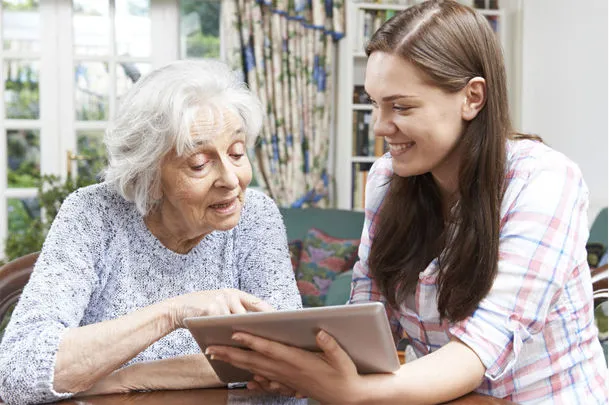 Alte und junge Frau sitzend am Tisch mit Tablet